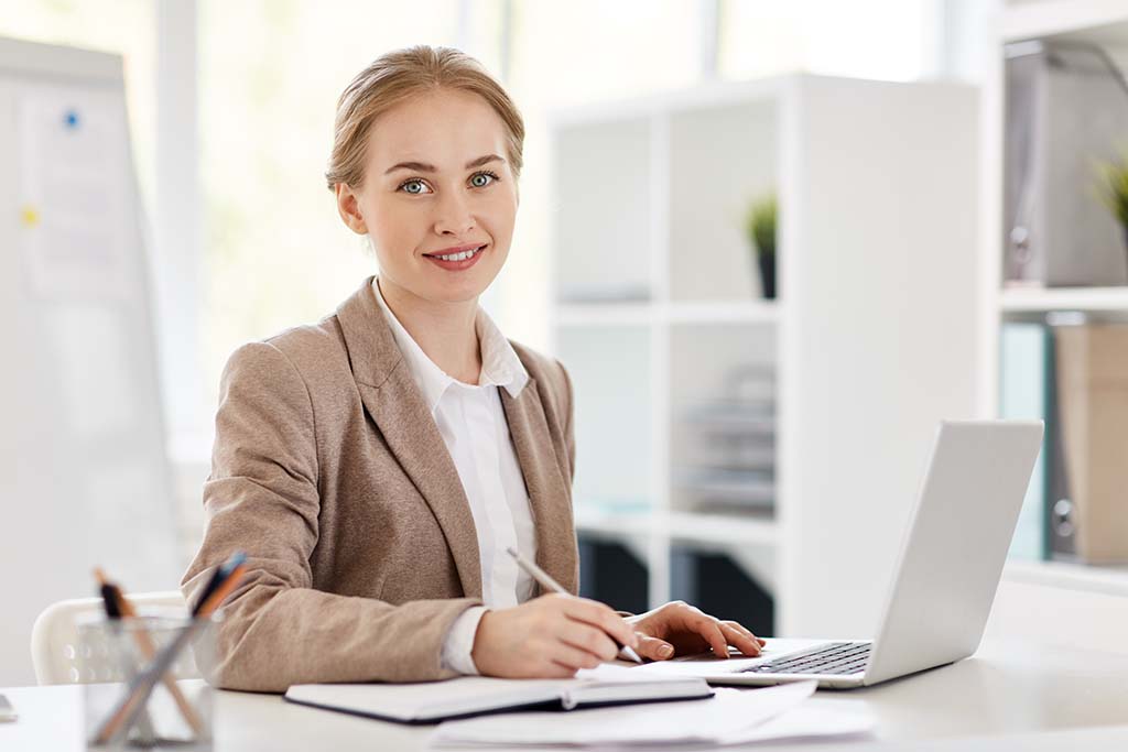 Pretty young accountant sitting by desk, planning work and browsing in the net