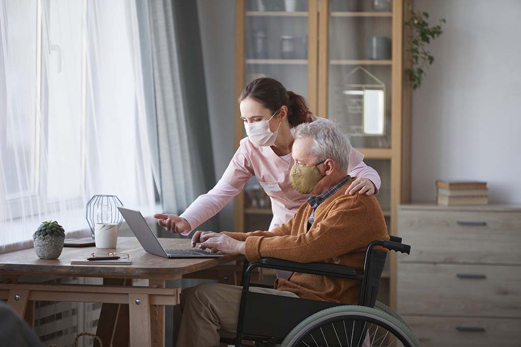 senior care consultant helps elderly man in wheelchair with laptop